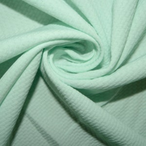 Puede incluir: Primer plano de una tela de punto de waffle verde claro. La tela es suave y texturizada, con un brillo sutil.