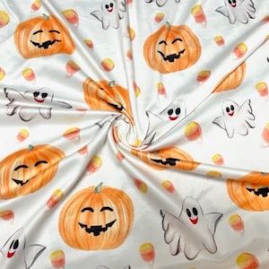 May include: White fabric with a repeating pattern of orange pumpkins with jack-o-lantern faces, white ghosts with smiling faces, and yellow and orange candy corn.