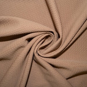 May include: A close-up of a brown textured fabric with a soft, crinkled appearance. The fabric is folded and draped, creating a smooth, flowing curve.