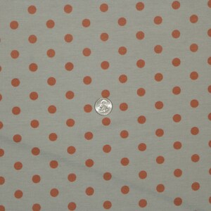 May include: A close-up of a light gray fabric with a repeating pattern of small, evenly spaced, orange polka dots.