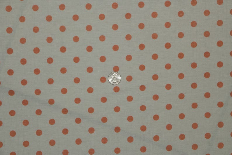 May include: A close-up of a light gray fabric with a repeating pattern of small, evenly spaced, orange polka dots.