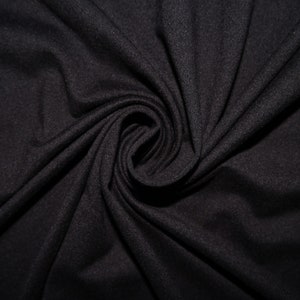 May include: Close-up of a black fabric with a soft, textured appearance. The material is draped and swirled, creating a spiral pattern in the center. The fabric's dark color and subtle texture suggest it could be used for clothing or home decor.