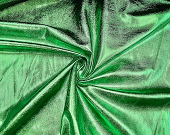 May include: A close-up of a green metallic fabric with a shiny, iridescent finish. The fabric is draped and folded, creating a textured and abstract pattern.