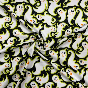 May include: White ghost pattern fabric on a black background. The ghosts have orange mouths and black eyes, outlined in green. The fabric is likely for Halloween-themed crafts or apparel.