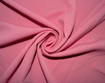 May include: Close-up of a swirl of pink fabric. The material has a textured, dimpled surface, creating a subtle pattern. The fabric is arranged in a spiral, with the center of the swirl visible. The color is a soft, muted pink.