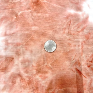 May include: A close-up of a tie-dye fabric in shades of white and orange. A US quarter is placed on the fabric to show the scale.