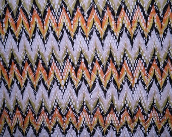May include: A close-up of a fabric with a chevron pattern in shades of orange, yellow, black, and white.