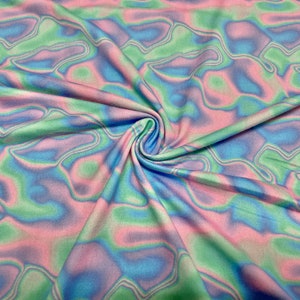 May include: Close-up of a fabric with a swirling pattern in pastel colours. The fabric features a blend of pink, blue, and green hues, creating a soft, flowing design. The fabric is gathered in the centre, showing the texture and drape of the material.