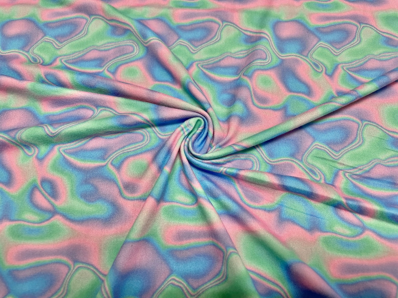 May include: Close-up of a fabric with a swirling pattern in pastel colours. The fabric features a blend of pink, blue, and green hues, creating a soft, flowing design. The fabric is gathered in the centre, showing the texture and drape of the material.
