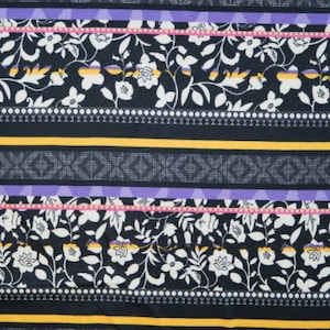 Op de afbeelding: Een zwarte stof met een herhalend patroon van witte bloemen en bladeren. De stof heeft een gestreept ontwerp met gele, paarse en roze accenten.