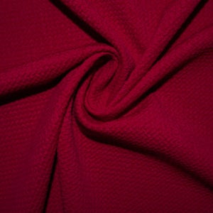 May include: A close-up of a deep red fabric with a textured waffle weave pattern. The fabric is folded and draped, showcasing its soft and luxurious feel.