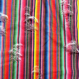 K&ouml;nnte beinhalten: Nahaufnahme eines farbenfrohen Stoffes mit Streifen und einem Used-Look-Design. Der Stoff weist vertikale Streifen in Rot, Orange, Gelb, Gr&uuml;n, Blau und Lila auf. Der Stoff hat ausgefranste Bereiche, die Textur und visuelles Interesse hinzuf&uuml;gen.