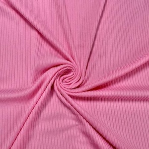 May include: Close-up of a pink ribbed knit fabric. The fabric is folded and swirled, creating a spiral pattern in the center. The vertical ribs run the length of the fabric, giving it a textured appearance.