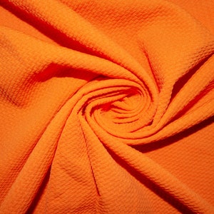 Puede incluir: Tela de color naranja brillante con un patrón texturizado similar a un gofre. La tela está dispuesta en un patrón arremolinado, creando un efecto visual dinámico. El color es un naranja vibrante y sólido.