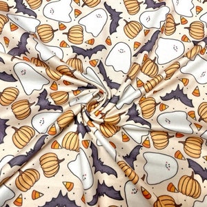 May include: A cream-colored fabric with a repeating pattern of orange pumpkins, white ghosts, and purple bats. The pattern is set against a light beige background.
