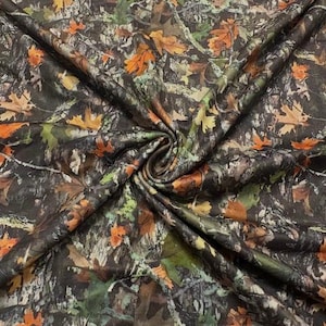 May include: A fabric featuring a detailed camouflage pattern with a forest floor motif. The design includes realistic depictions of fallen autumn leaves in shades of orange, yellow, and brown, interspersed with dark green foliage and textured bark.