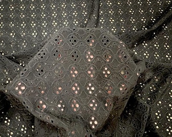 May include: Close-up of black eyelet fabric with a repeating floral pattern. The fabric is folded, revealing the texture and openwork design. The eyelet holes are small and evenly spaced, creating a delicate and airy appearance. The fabric is likely cotton or a cotton blend.