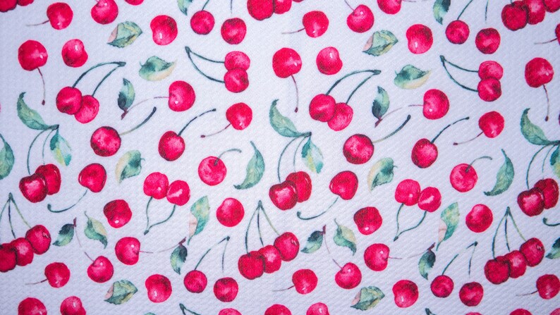 Puede incluir: Una tela con un patr&oacute;n repetido de cerezas rojas brillantes y hojas verdes sobre un fondo blanco. Las cerezas tienen un efecto de acuarela y el dise&ntilde;o est&aacute; uniformemente espaciado en la tela.