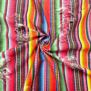 K&ouml;nnte beinhalten: Nahaufnahme eines lebendigen Stoffes mit vertikalen Streifen in Rot, Orange, Gelb, Gr&uuml;n, Blau und Lila. Der Stoff hat ein strukturiertes Aussehen mit ausgefransten Kanten, was einen rustikalen Look erzeugt. Der Stoff ist in der Mitte zusammengekn&uuml;llt.