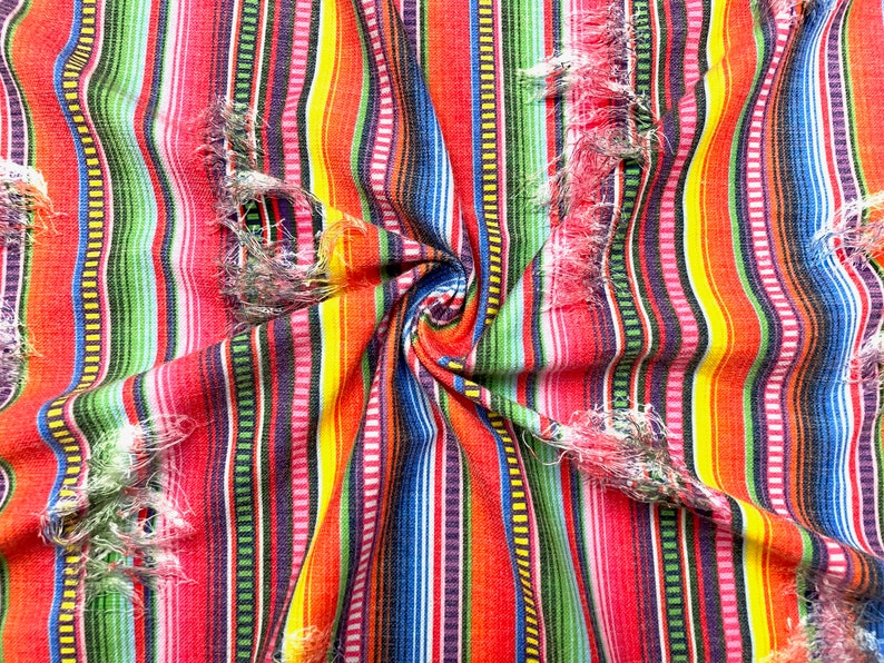 K&ouml;nnte beinhalten: Nahaufnahme eines lebendigen Stoffes mit vertikalen Streifen in Rot, Orange, Gelb, Gr&uuml;n, Blau und Lila. Der Stoff hat ein strukturiertes Aussehen mit ausgefransten Kanten, was einen rustikalen Look erzeugt. Der Stoff ist in der Mitte zusammengekn&uuml;llt.
