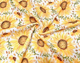 May include: Close-up of a fabric with a repeating pattern of watercolor sunflowers. The sunflowers are yellow with brown centers and green leaves, set against a white background. The fabric is folded, showing the texture and design.