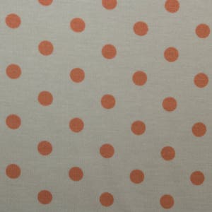 May include: A close-up of a light beige fabric with a repeating pattern of small, evenly spaced, coral-colored polka dots.