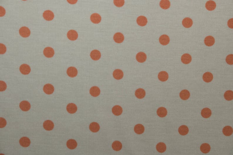 May include: A close-up of a light beige fabric with a repeating pattern of small, evenly spaced, coral-colored polka dots.
