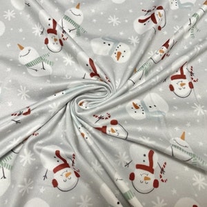 May include: White fabric with a repeating pattern of snowmen wearing scarves and hats. The background is a light gray with white snowflakes.