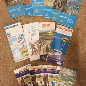 May include: A collection of vintage travel guides and maps, featuring states like Colorado, Oklahoma, and Pennsylvania. The guides have blue and white covers with illustrations and text, including the "Guide To" series and oil company logos.