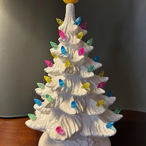 May include: A white ceramic Christmas tree with multi-colored lights and a yellow rubber duck on top.
