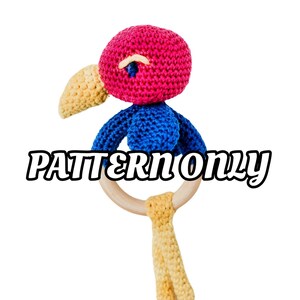 May include: A crocheted bird rattle toy with a pink head, blue body, and yellow beak. The toy is attached to a wooden ring.