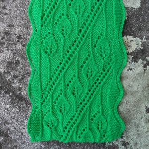 May include: A green knitted blanket with a lacy pattern. The blanket is made with a fine yarn and has a delicate, airy feel.