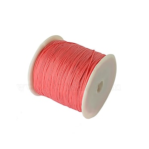 May include: A spool of pink waxed cotton cord, wound around a white plastic bobbin.