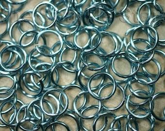 May include: A large pile of teal-colored metal jump rings. The rings are all the same size and are arranged in a random pattern.