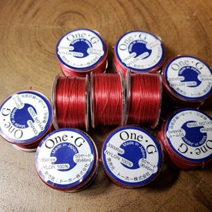 May include: Close-up of eight spools of red thread labeled "One.G Made in Japan" with different thread sizes and yardage amounts.