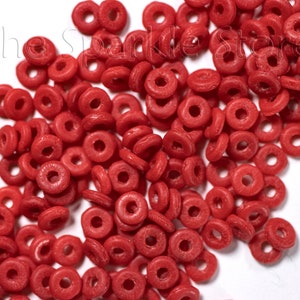 May include: A large pile of bright red plastic donut-shaped beads. The beads are scattered on a white surface.