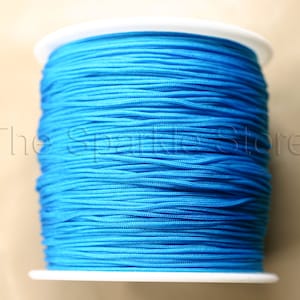 May include: A spool of bright blue elastic cord. The cord is wound tightly around a white plastic spool.