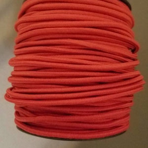May include: A spool of red elastic cord, wound tightly and ready for use in crafting projects.