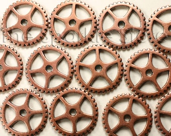 May include: Close-up of several small, copper-colored metal gears. Each gear has a circular shape with a toothed outer edge and a five-spoke design in the center. The gears are evenly spaced.