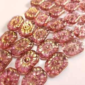Könnte beinhalten: Eine Sammlung von rosa und goldenen Glasperlen mit Blumenmuster. Die Perlen sind oval geformt und haben eine strukturierte Oberfläche.