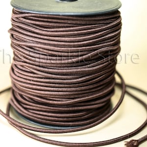 May include: A spool of brown elastic cord. The cord is wound tightly around the spool and is ready to be used for sewing or crafting projects.