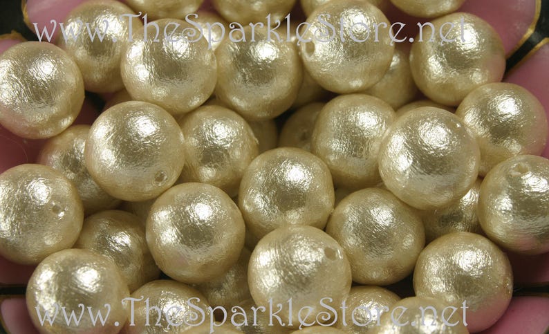 May include: A close-up image of a bowl filled with ivory-colored pearl-like beads. The beads have a textured surface and a subtle shimmer. The beads are arranged in a random pattern, creating a visually appealing display.