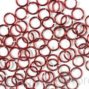 May include: A large pile of red jump rings. The rings are made of metal and are about 1/2 inch in diameter.