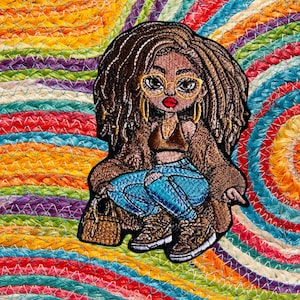 Può includere: Toppa ricamata di una donna con capelli castani e una giacca marrone, che indossa jeans blu e occhiali. Tiene una borsa marrone e ha uno sfondo colorato.