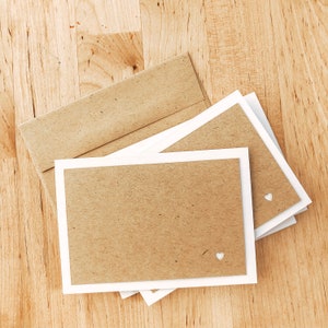 May include: Two brown kraft paper cards with white borders and white heart cutouts. The cards are stacked on top of a brown envelope.