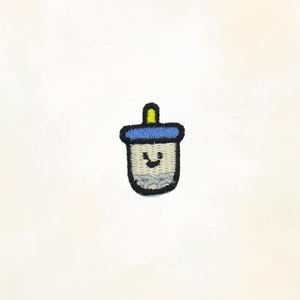 May include: Embroidered patch of a smiling boba tea cup. The patch features a blue lid, a yellow straw, and a gray cup with a smiling face. The patch is on a white background.