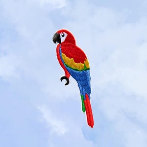 May include: Embroidered patch of a vibrant macaw parrot. The bird features a red head and body, yellow and blue wings, and a blue tail. The patch is set against a light blue sky background.