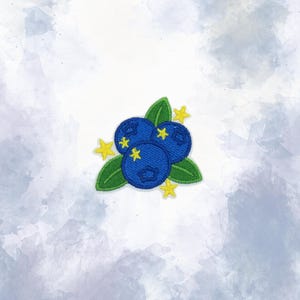 May include: An embroidered patch featuring three dark blue blueberries with green leaves and small yellow stars scattered around the fruit. The design is stitched with visible thread texture and defined borders on a white background.