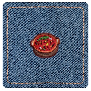May include: A square denim patch with orange stitching around the border. Centered on the blue fabric is an embroidered design of a brown cooking pot filled with red stew, topped with green scallions and small yellow and dark brown pieces.