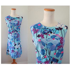 May include: A sleeveless knee-length dress in a light blue color featuring a vibrant floral pattern in shades of dark blue, purple, and bright pink. The bodice includes a small fabric bow detail at the neckline and a horizontal seam across the chest.
